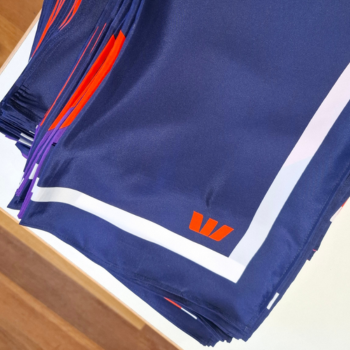 Folded navy fabric panels with a white border and orange logo, fringed edges in orange and purple visible in the background.